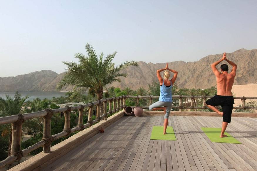 man and woman practicing yoga outside at Six Senses Zighy Bay