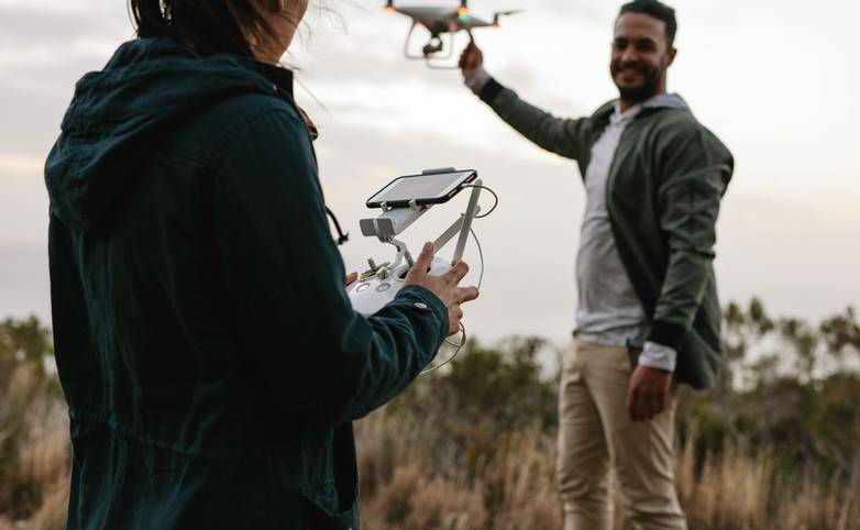 Woman with remote control and  man holding a flying drone in countryside. Young couple flying drone in countryside.