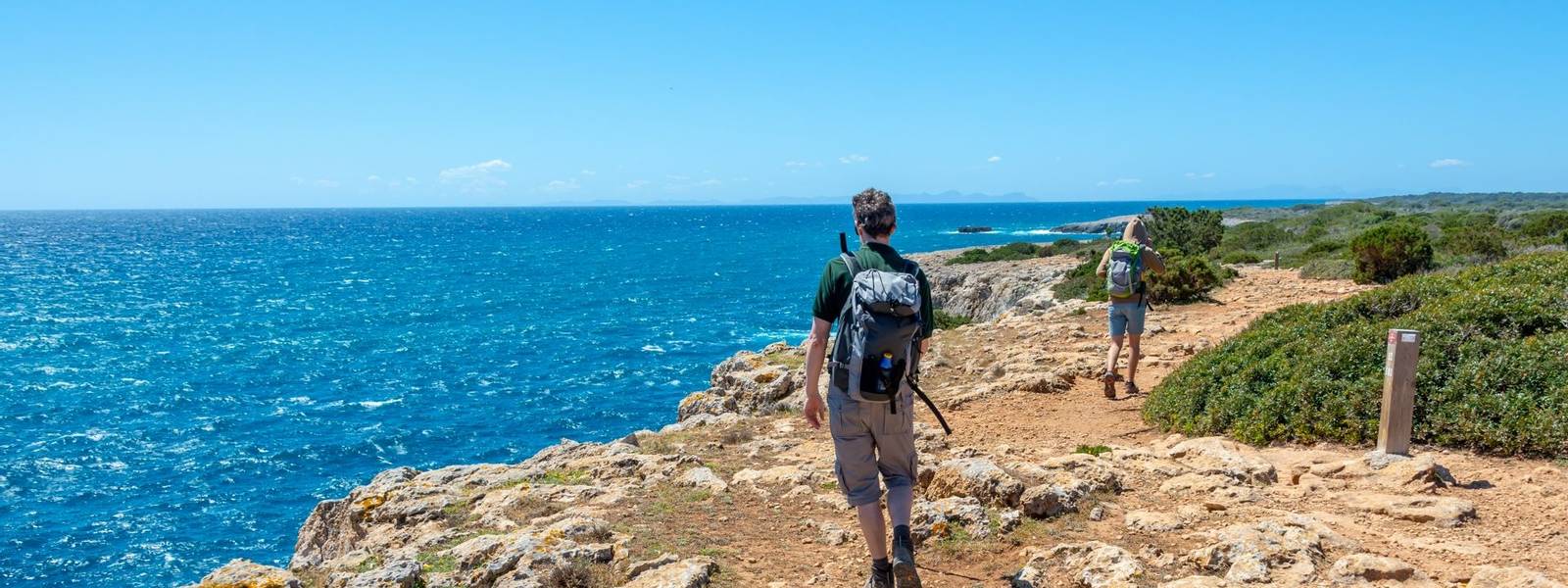 Hikers on a coastal path by the sea in Menorca, Balearic islands, Spain