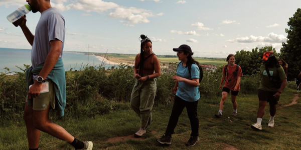 Group photo of 30+ HF Holidays guests, posing for the photo with a large green banner that reads 'HF Holidays: Walk Your Way'