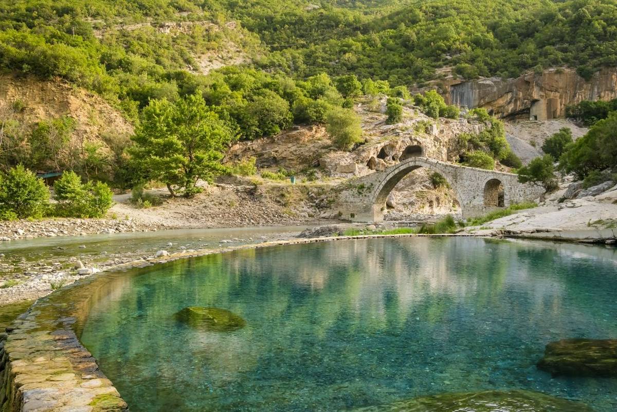 Benja Thermal Baths in Permet, Albania. Pool with hot water and old arch shape stone bridge at background. Popular tourist d…