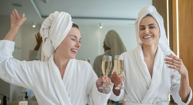 Spa weekend. Two pretty girls in white robes drinking champagne and enjoying