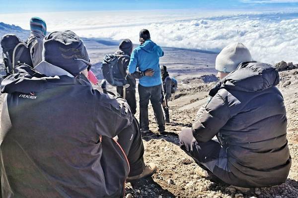 Hikers standing in a line over a wide vista holding their arms wide in celebration on the trek to Kilimanjaro