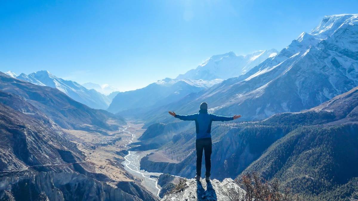 Man wearing a beanie and blue jumper, spreads his arms wide, breathing deeply the fresh mountain air. His gesture represents…