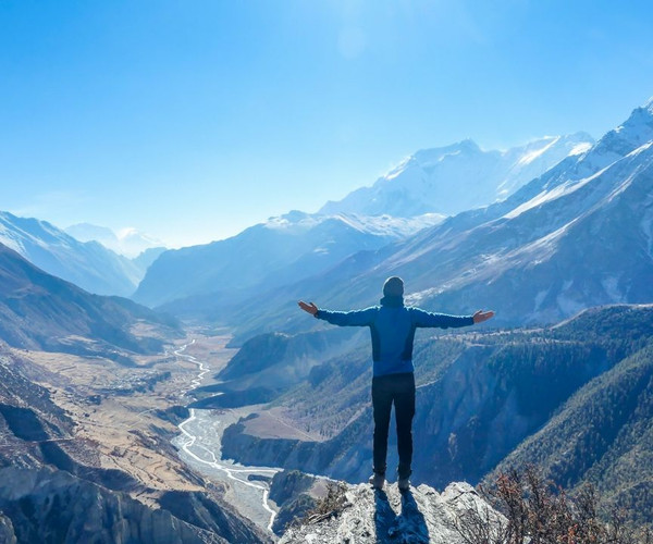 A man in blue with arms held high, looking out over the epic vistas of Nepal on the Annapurna Circuit