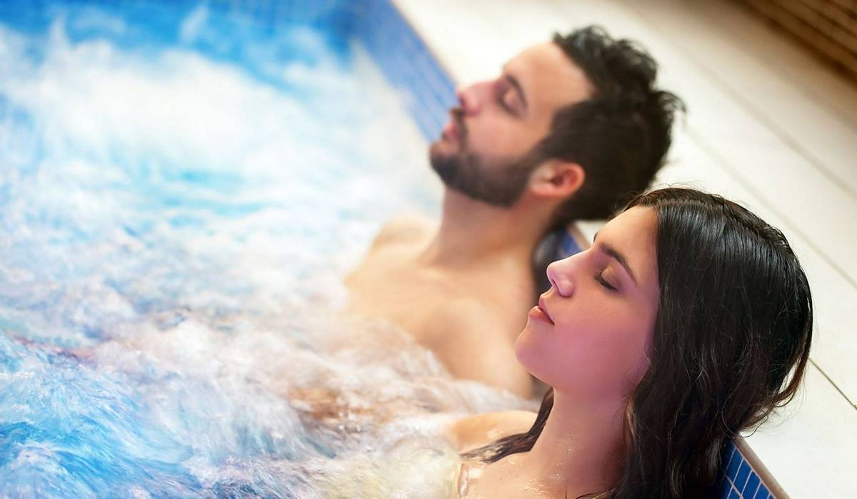 Close up portrait of young couple relaxing in spa jacuzzi. Couple together in bubble water with eyes closed.
