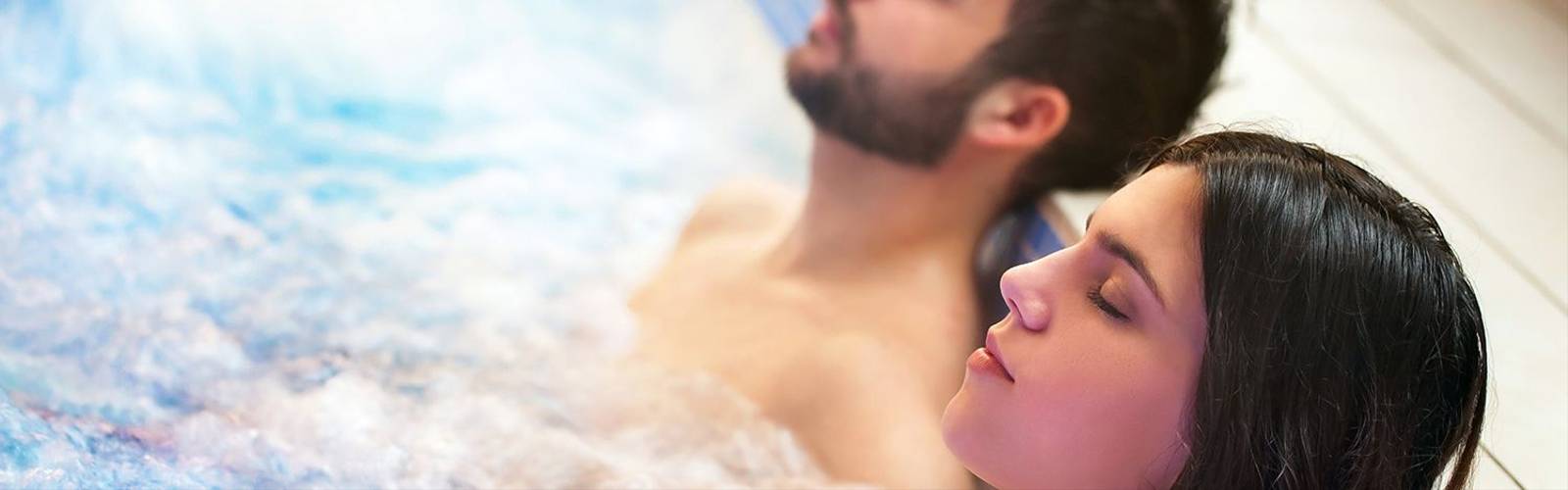 Close up portrait of young couple relaxing in spa jacuzzi. Couple together in bubble water with eyes closed.