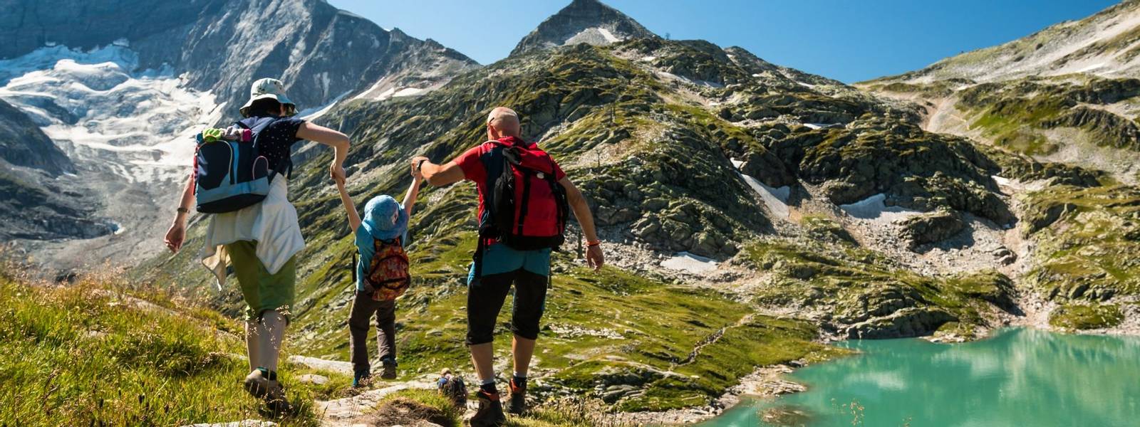 family with child hiking on holiday in austrian alps with lake and glacier view