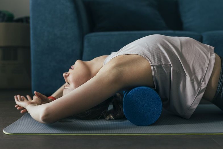 Beautiful fit woman exercising with a blue foam roller at home, pilates concept.
