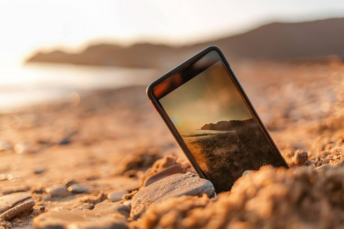 The concept of the photos on the phone. The smartphone lies buried in the sand on the beach, and takes a photo of the beach …