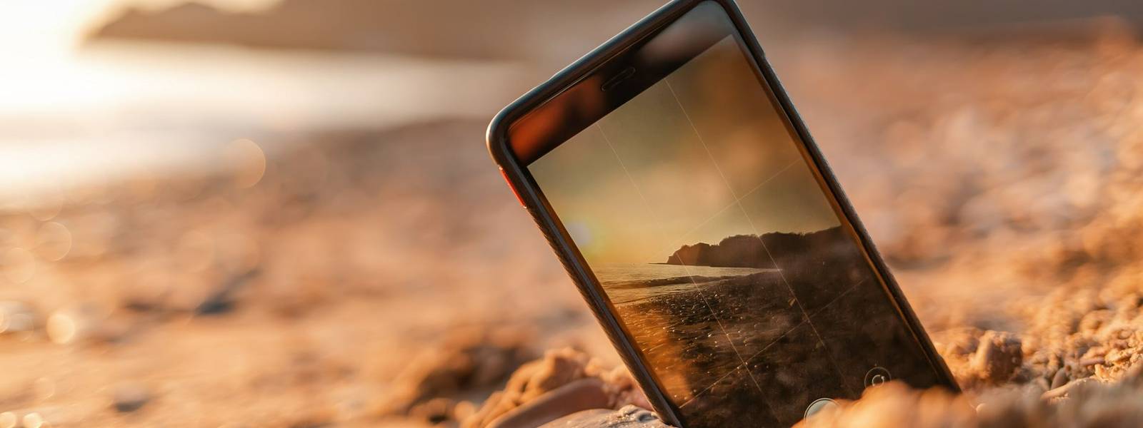 The concept of the photos on the phone. The smartphone lies buried in the sand on the beach, and takes a photo of the beach …