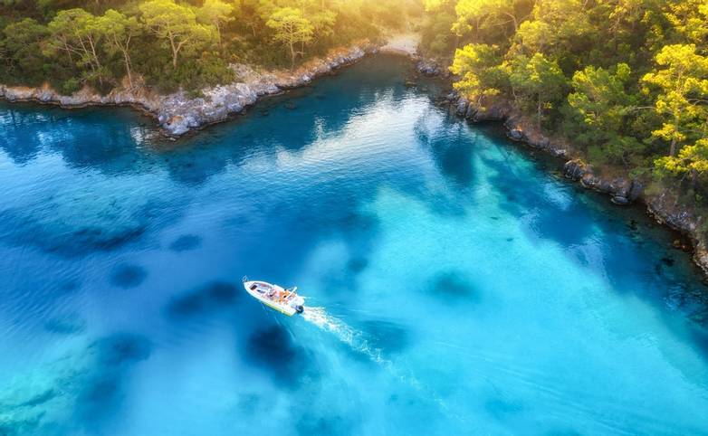 Speed boat on blue sea at sunrise in summer. Aerial view of motorboat in blue lagoon, rocks in clear azure water. Tropical l…
