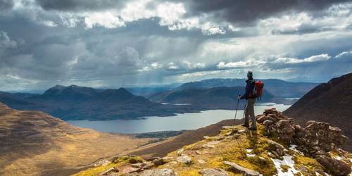 Walker standing on the slopes of a mountain looking down onto a lake in Scotland