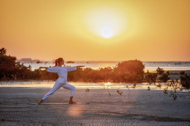 Woman practicing yoga on the beach at Zulal Wellness Resort in Qatar