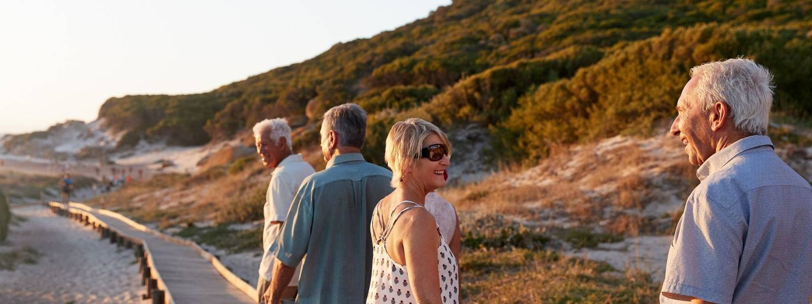 Group Of Senior Friends Walking Along Boardwalk At Beach On Summer Group Vacation