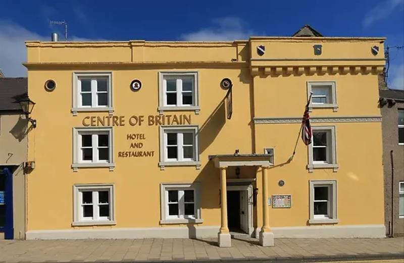 Mustard yellow-coloured hotel with 'CENTRE OF BRITAIN' written above the door.
