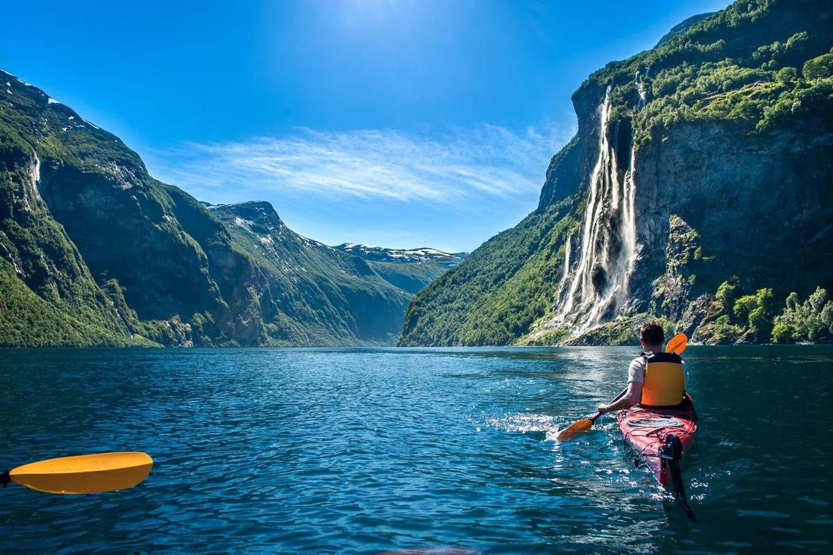 young man kayaking along the fjord geiranger enjoying the waterfall 