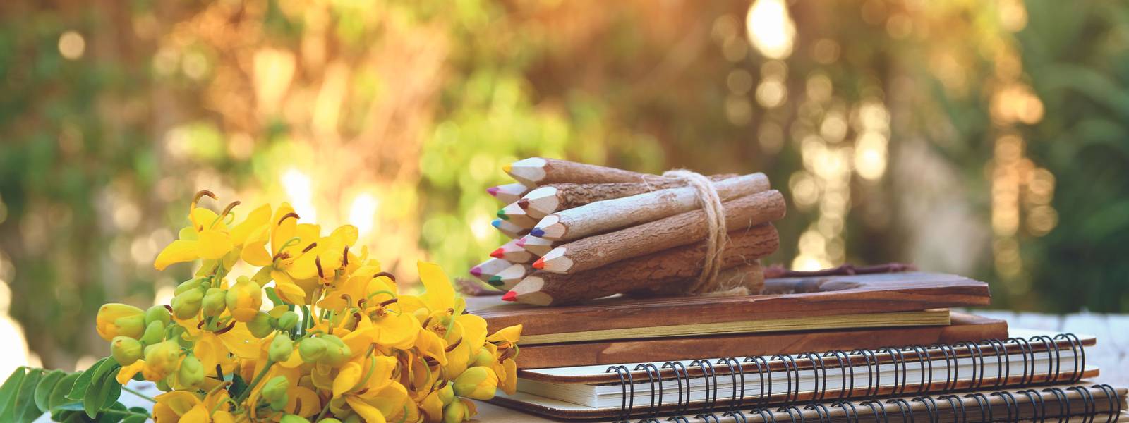 Image of notebooks, colorful pencils on wooden table outdoors at afternoon. selective focus