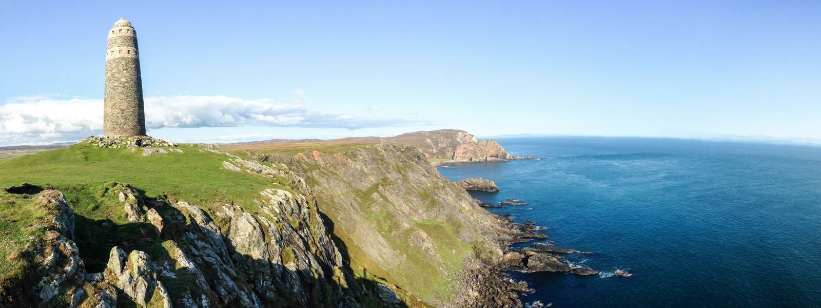 A large rock tower sits on a grassy field at the tip of the Oa Peninsula on the island of Islay in Scotland.