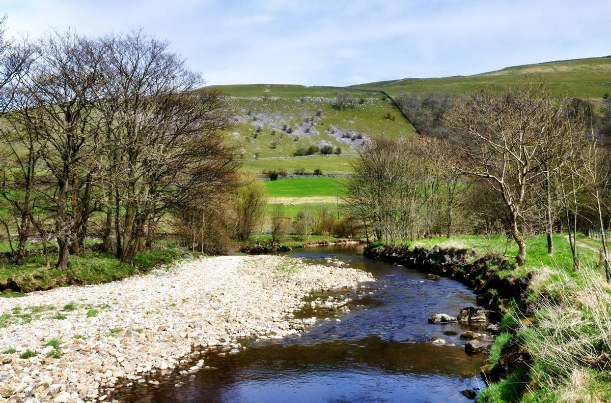 View of the River Wharf with tree bordered banks, against a hilly background in the Yorkshire Dales, England.