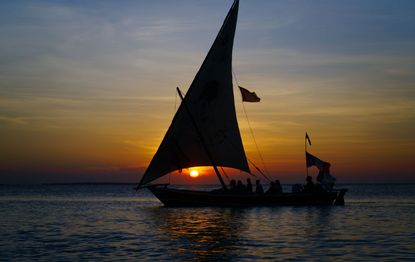 dhow boat sailing with people against the setting sun and cloudy sky. High quality photo