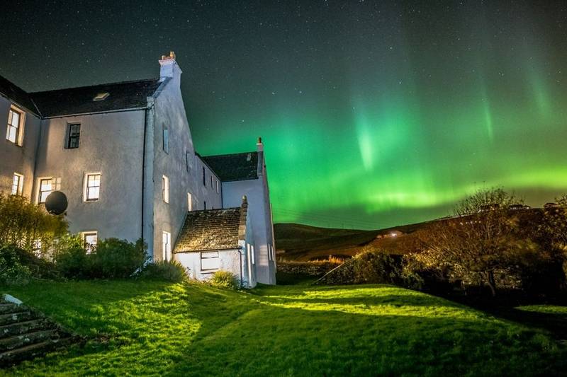 White hotel in the foreground, with the Northern Lights illuminating the sky a rich green colour.