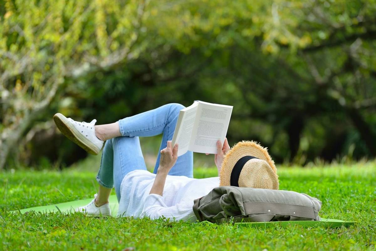 Happy woman lying on green grass reading a book in the park( outdoors )
