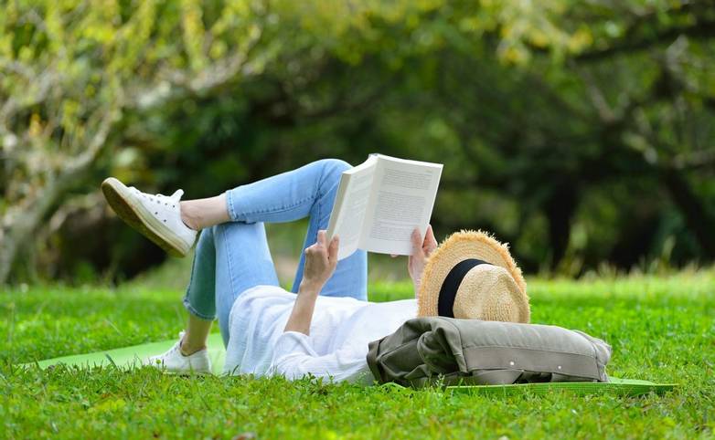 Happy woman lying on green grass reading a book in the park( outdoors )