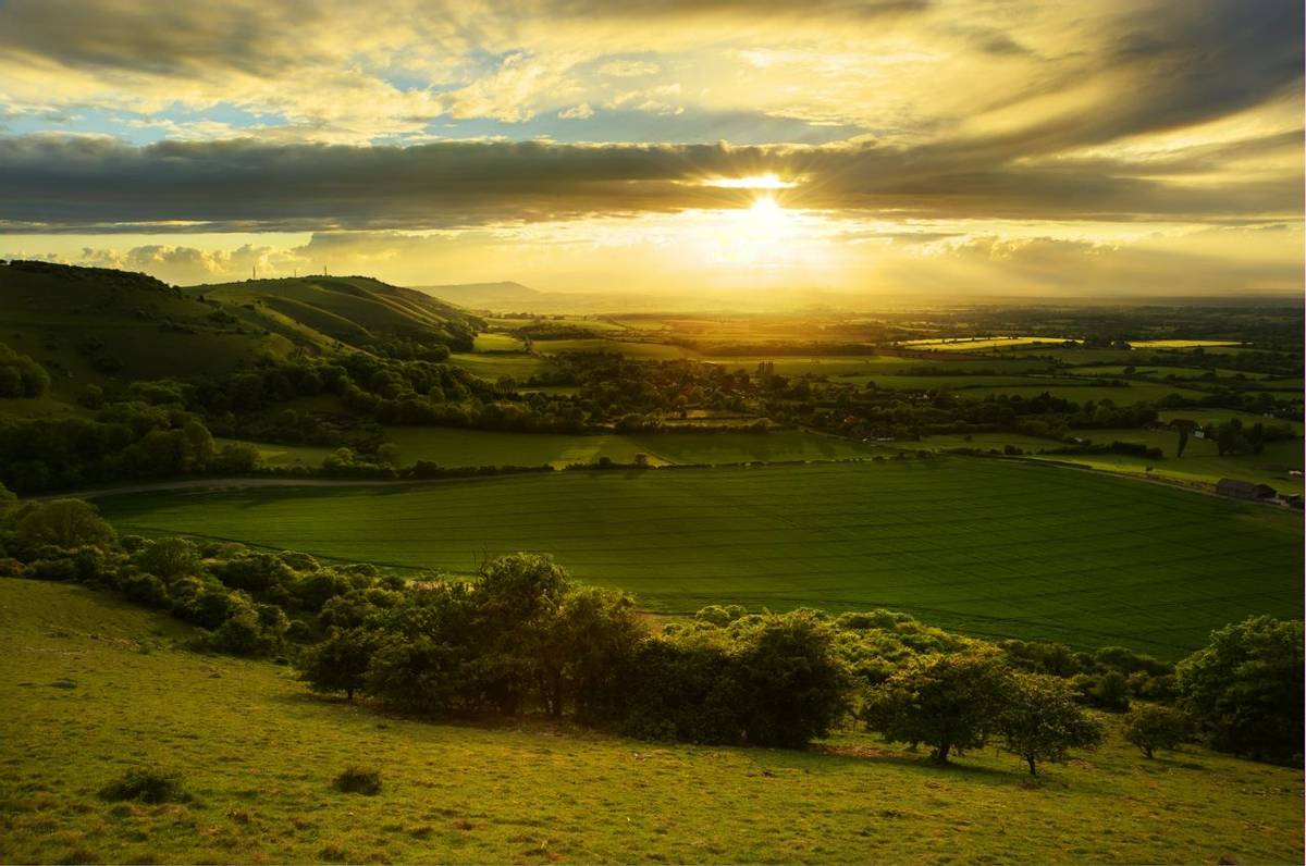 Stunning countryside landscape with sun lighting side of hills at sunset