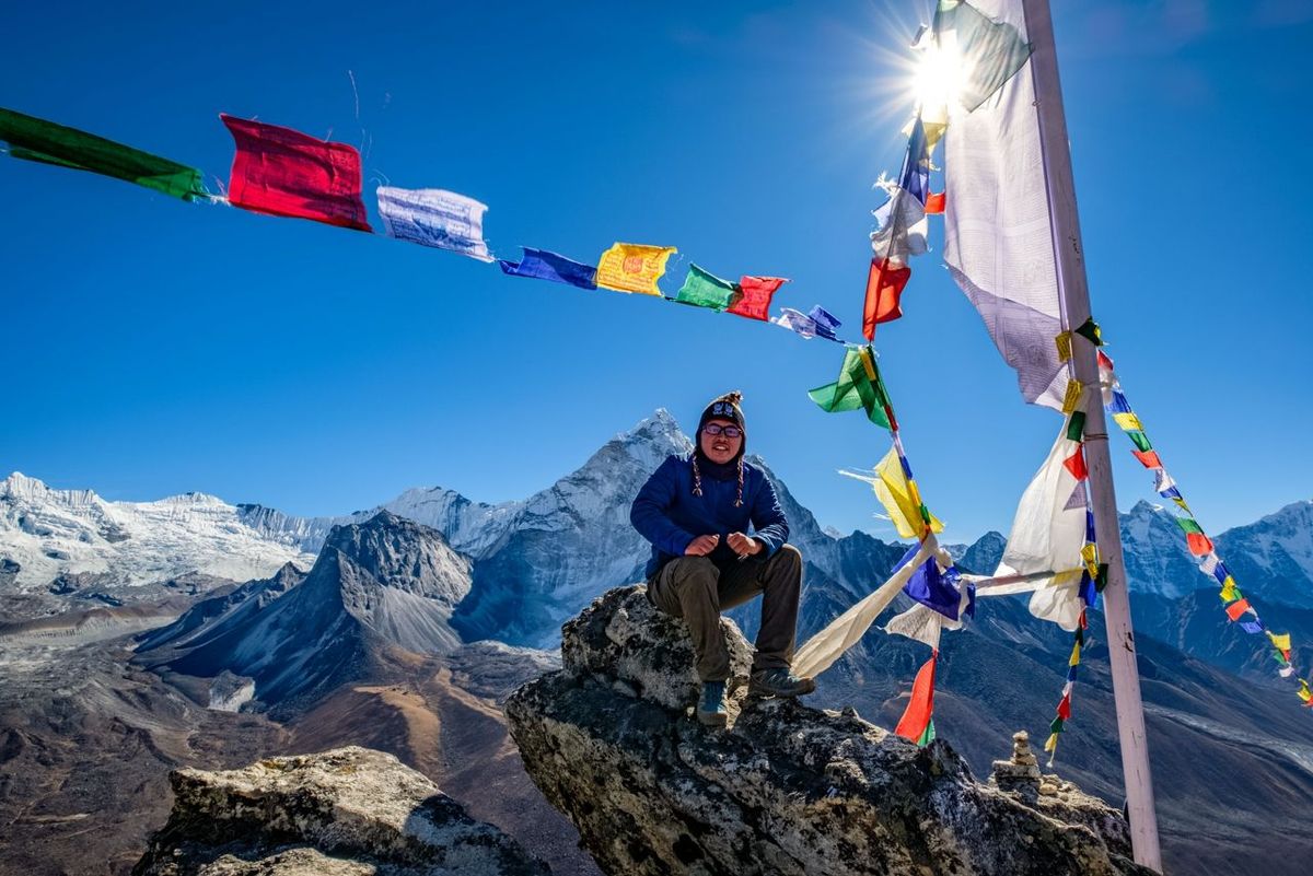 Asian hiker sitting on the cliff in Nangkartsang Peak, Everest Base Camp, with clear blue sky and himalayan mountain range a…