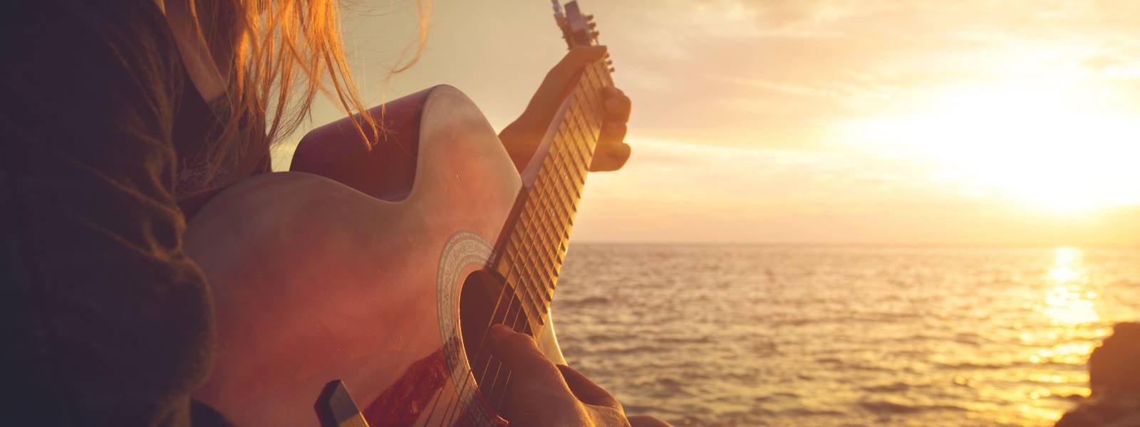 Beautiful young woman playing guitar on sunset beach
