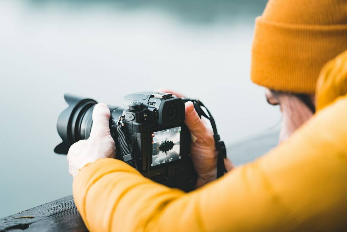 Close up view of male photographer using the rear lcd screen to compose and take a landscape photo with his digital camera d…