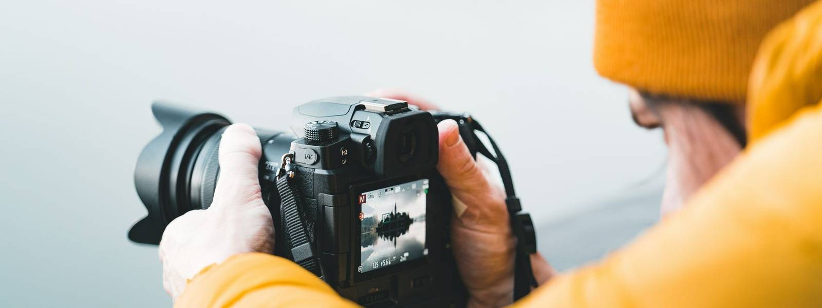 Close up view of male photographer using the rear lcd screen to compose and take a landscape photo with his digital camera d…