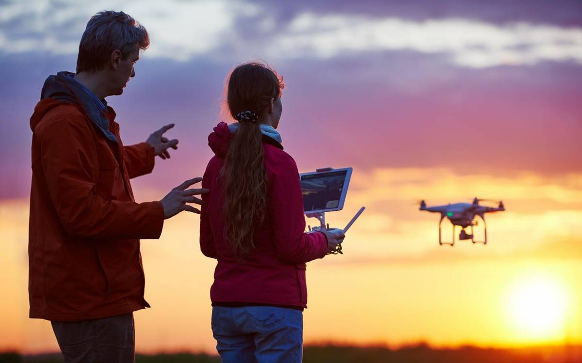 Man with child operating drone flying or hovering by remote control in sunset.
