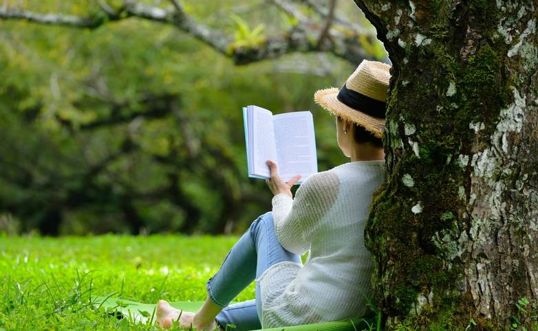 Middle aged woman sitting under a tree reading a book in the park