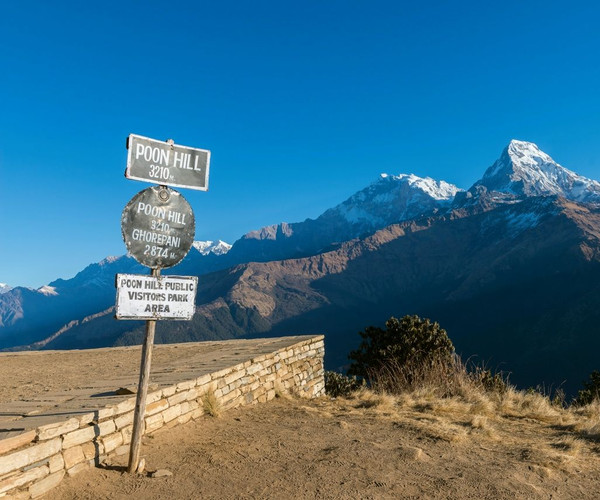 A rugged sign post in front of snowcapped peaks marking the way to Annapurna Poon Hill in Nepal