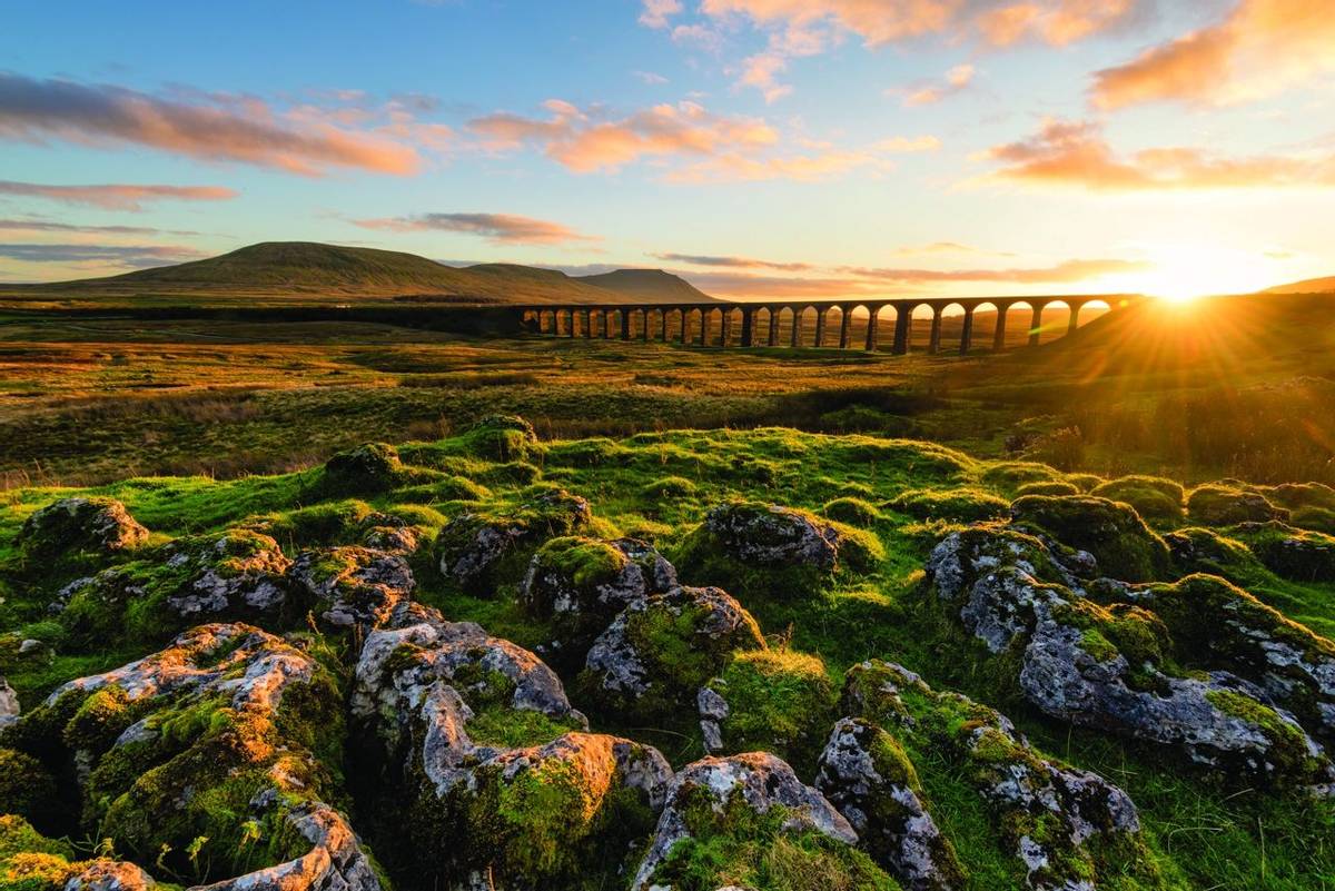 Gorgeous golden light as the sun sets behind the Ribblehead Viaduct with rocks in foreground.