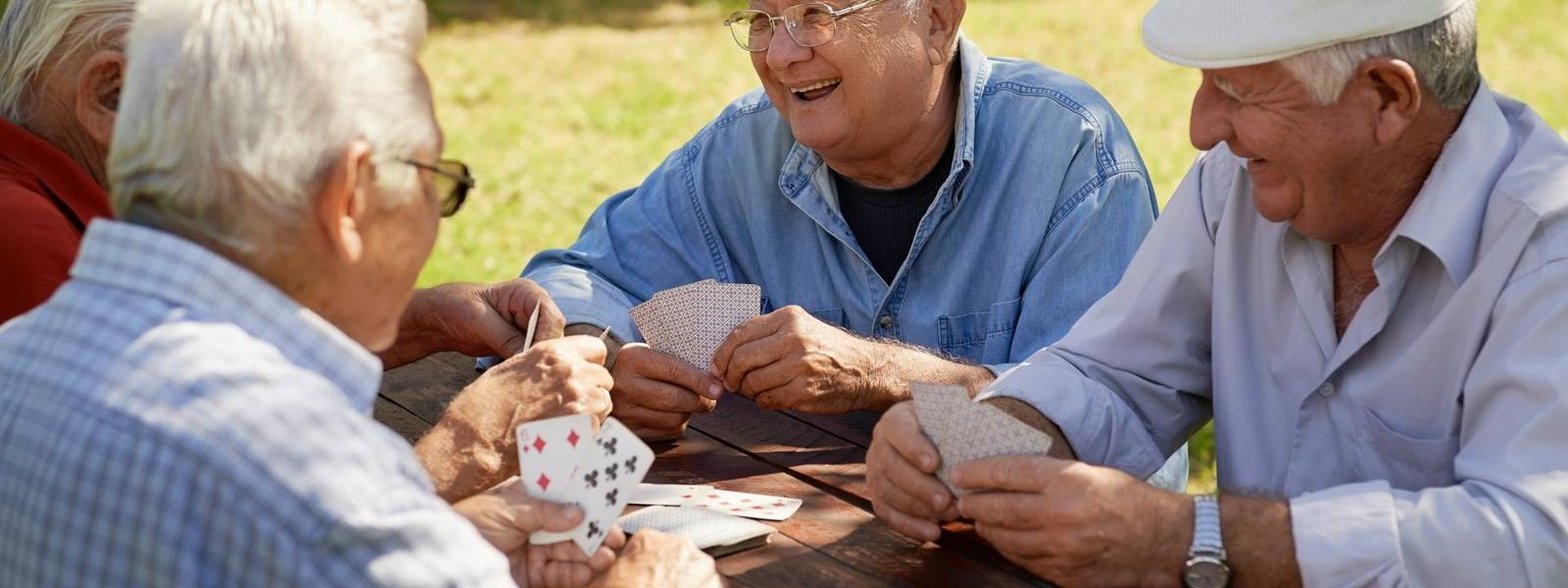 Active retirement, old people and seniors free time, group of four elderly men having fun and playing cards game at park. Wa…