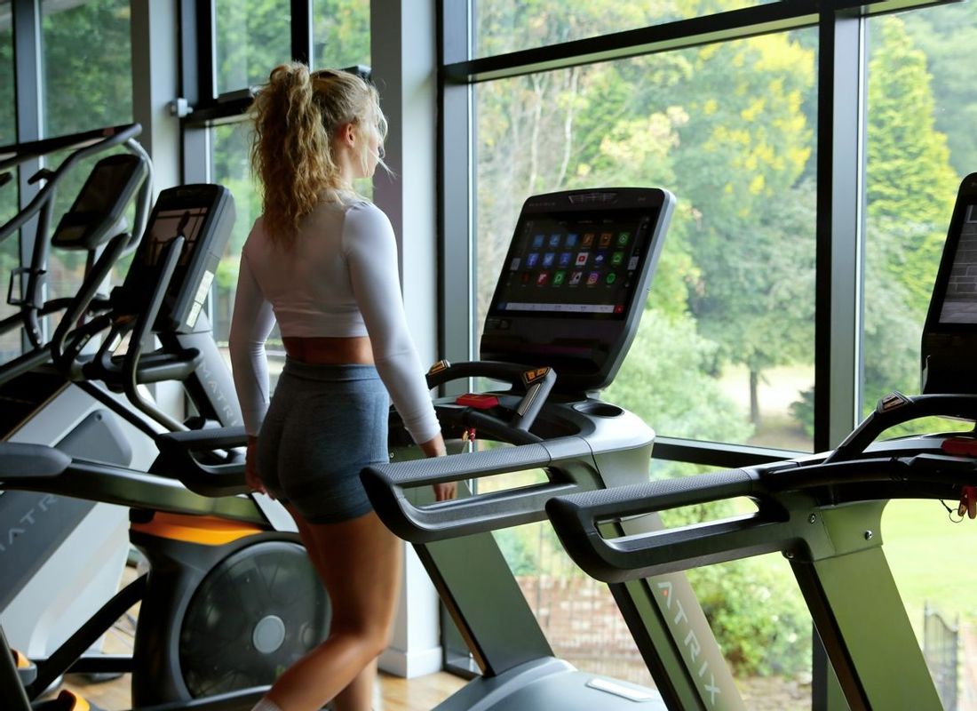 Woman in hotel gym using treadmill looking out to beautiful view of the Hampshire countryside.