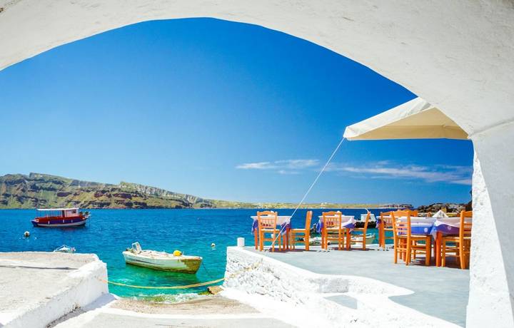 The old harbor of Ammoudi under the famous village of Oia at Santorini, Greece through a frame of an old arched building. The old harbor of Ammoudi under the famous village of Oia at Santorini, Greece through a frame of an old arched building.