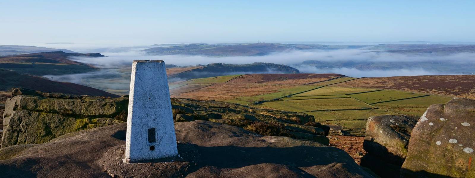 Beside the triangulation station on Stanage Edge looking across Derbyshire on a misty spring morning