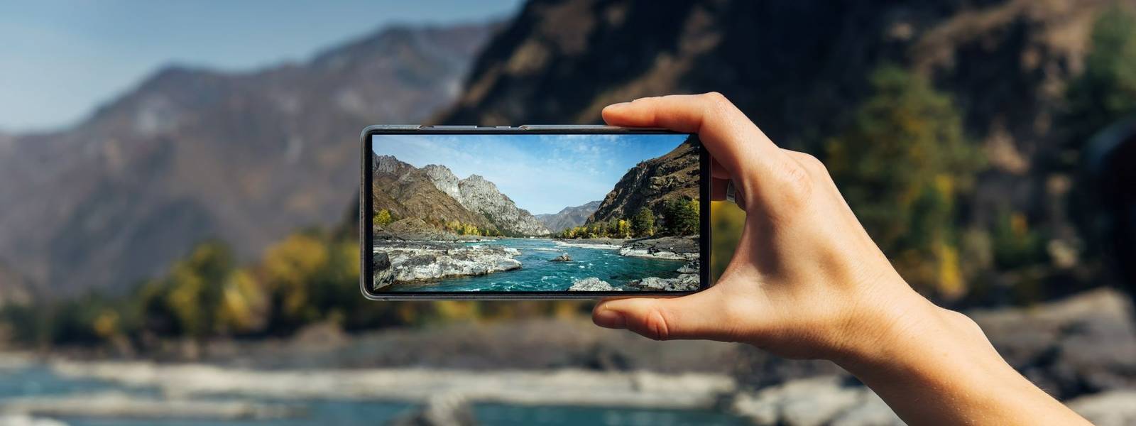 Female hand with smartphone close-up. Taking photo on smartphone while traveling. Delightful mountain landscape, stormy rive…