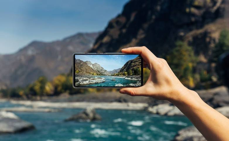 Female hand with smartphone close-up. Taking photo on smartphone while traveling. Delightful mountain landscape, stormy rive…