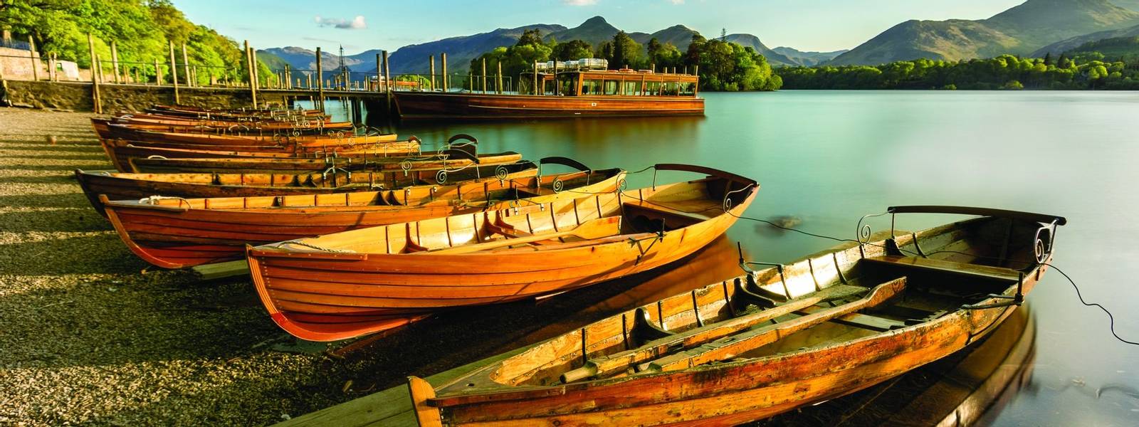 Wooden Rowing Boats lined up on shoreline being illuminated with golden light from the setting sun. Derwentwater, Lake Distr…