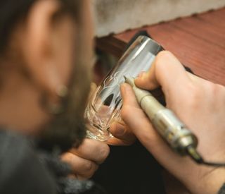 Rearview cropped close up of a craftsman engraving crystal glasses working on his workbench profession design art creating m…