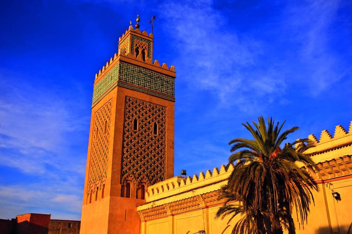 Ornate minaret rises from mosque walls into blue sky in Morocco