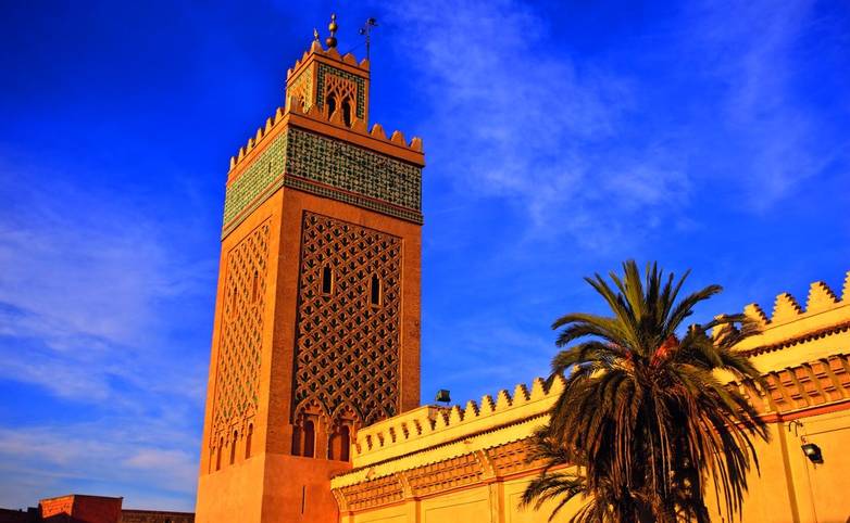 Ornate minaret rises from mosque walls into blue sky in Morocco