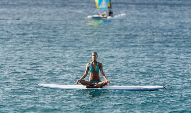 A Woman wearing blue bikini sitting on the paddle board that is floating on the sea