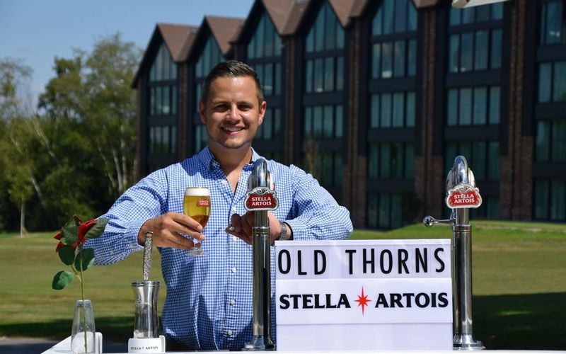 Man on golf course holding a freshly poured cold pint in front of self catering apartments
