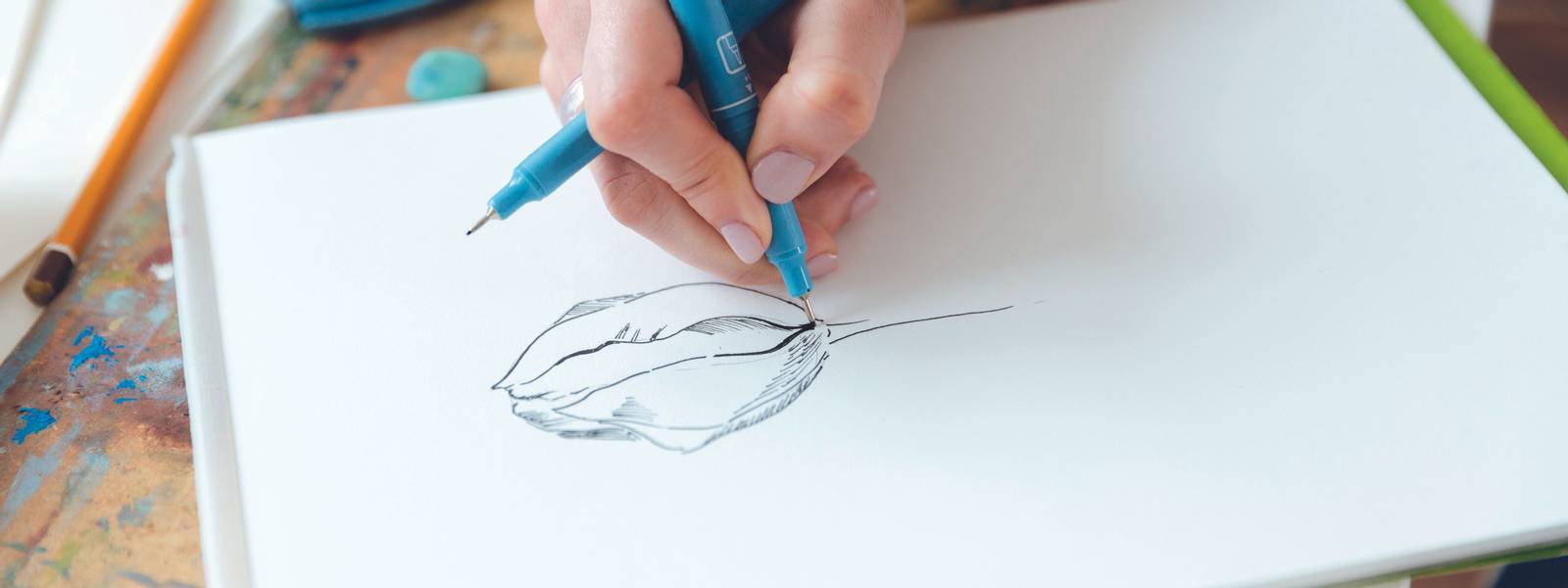 Closeup of hands of woman artist drawing with gel ink pen in sketchbook